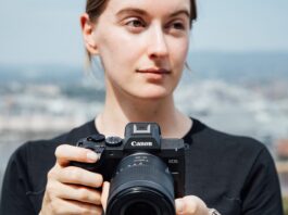 Canon EOS R8 Mark II : le plein format compact gagne la stabilisation Une photographe tient le Canon EOS R8 Mark II équipé d'un zoom RF devant un paysage urbain flou