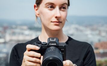 Une photographe tient le Canon EOS R8 Mark II équipé d'un zoom RF devant un paysage urbain flou