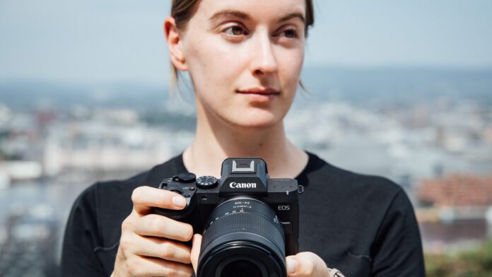 Une photographe tient le Canon EOS R8 Mark II équipé d'un zoom RF devant un paysage urbain flou