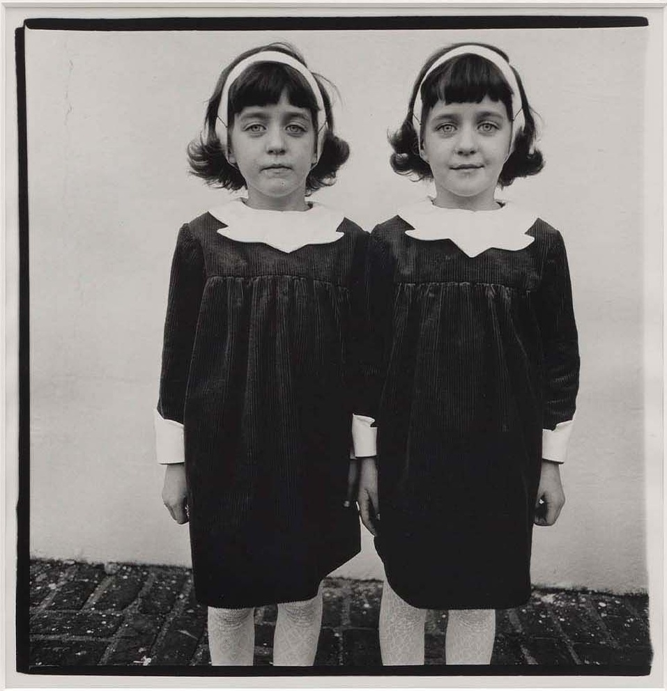 Deux jumelles identiques en robe sombre à col blanc et serre-tête, debout côte à côte, photographie de Diane Arbus (Roselle, 1967)