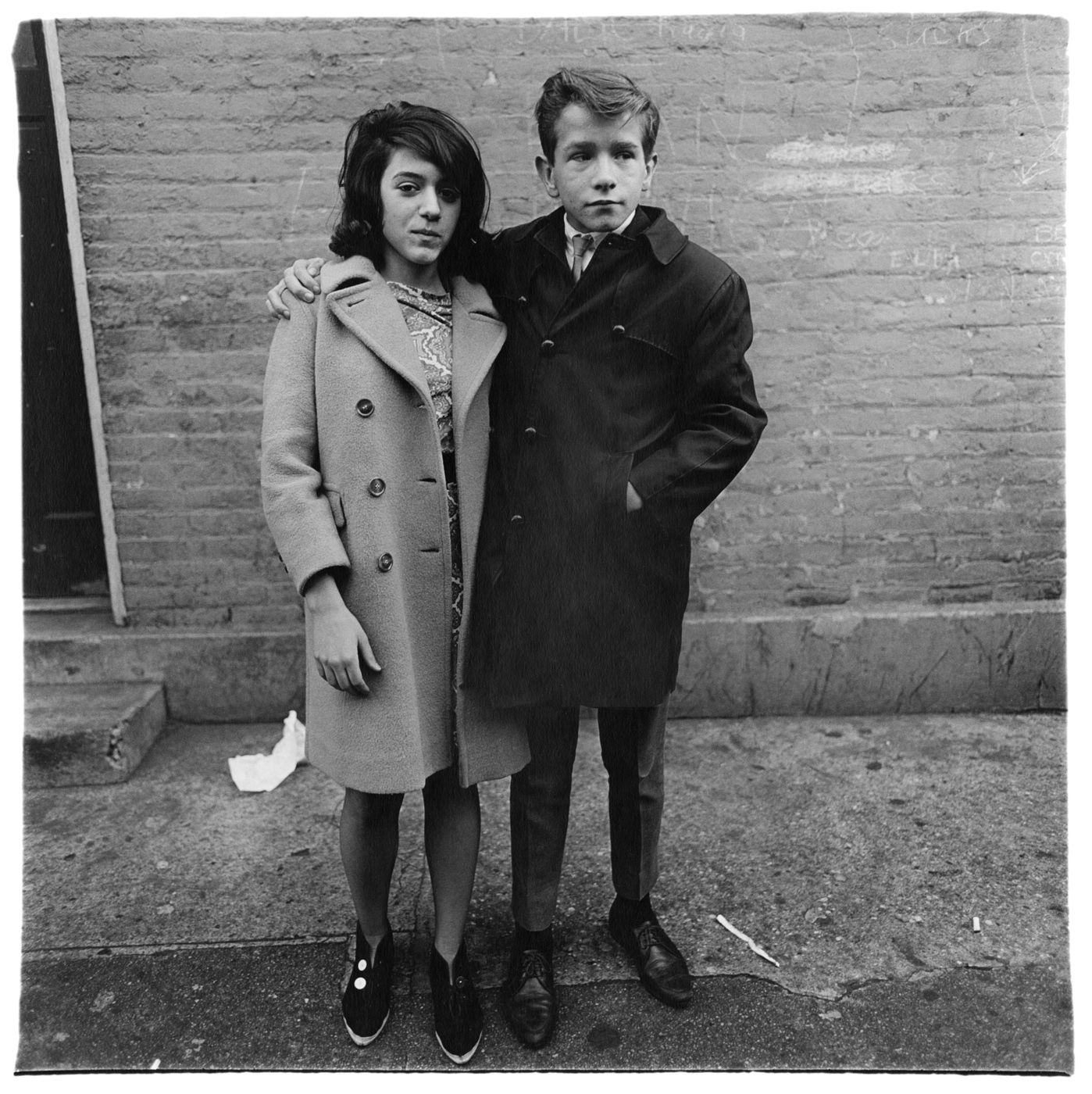 Couple d’adolescents en manteaux, enlacés sur un trottoir de Hudson Street à New York, photographie de Diane Arbus (1963)