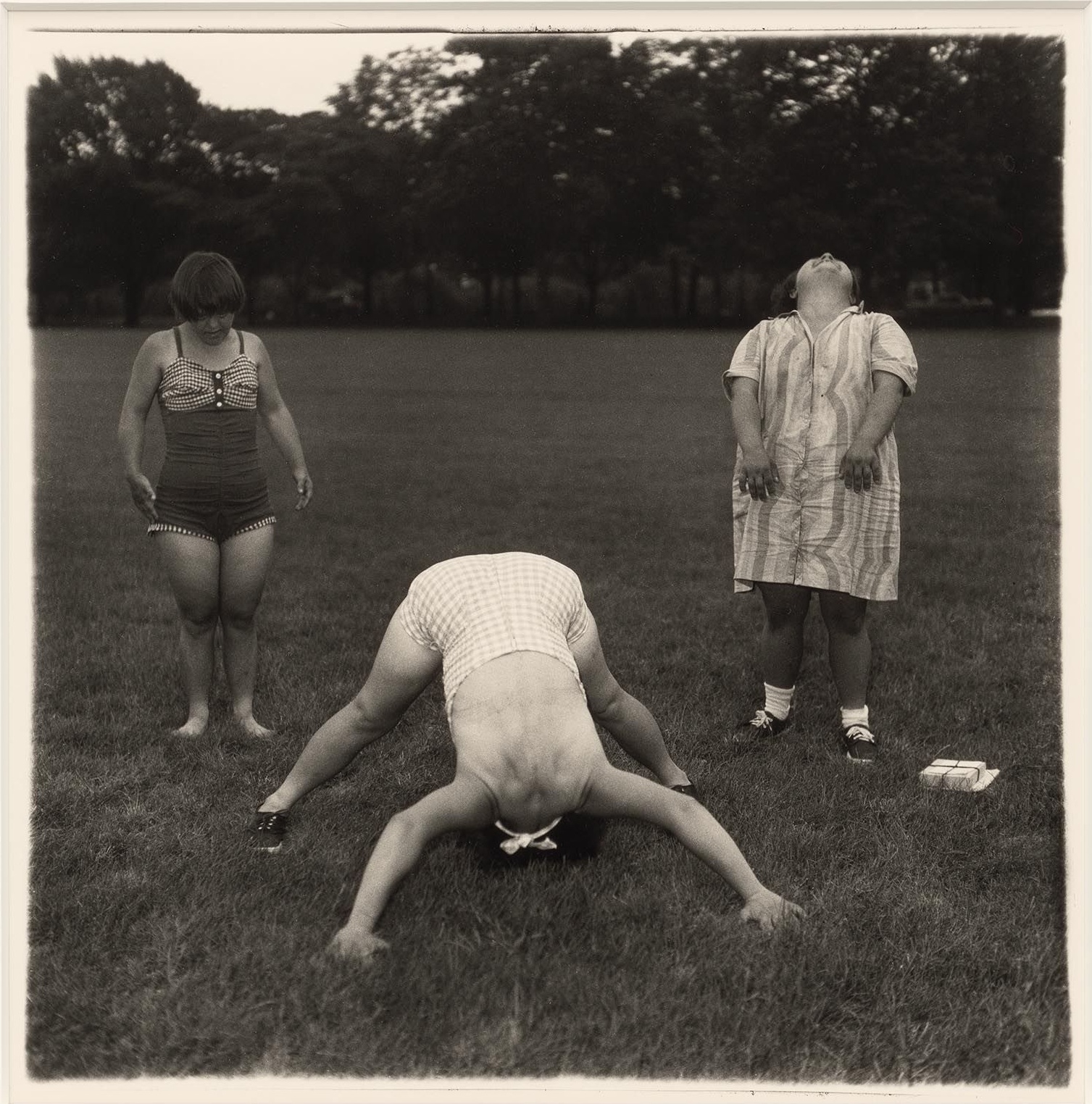 Trois femmes sur une pelouse, l’une penchée en avant la tête entre les jambes, série Untitled de Diane Arbus (1970-1971)