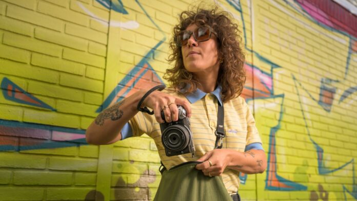 Nikon Z5IIC – photographe en ville devant un mur de graffitis Photographe tenant un Nikon Z5IIC argenté devant un mur couvert de graffitis
