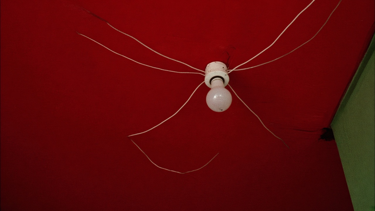 Plafond peint en rouge vif vu en contre-plongée, avec une ampoule nue et des fils électriques blancs